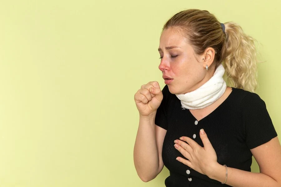 A woman wearing a neck brace, coughing due to an unknown cause.